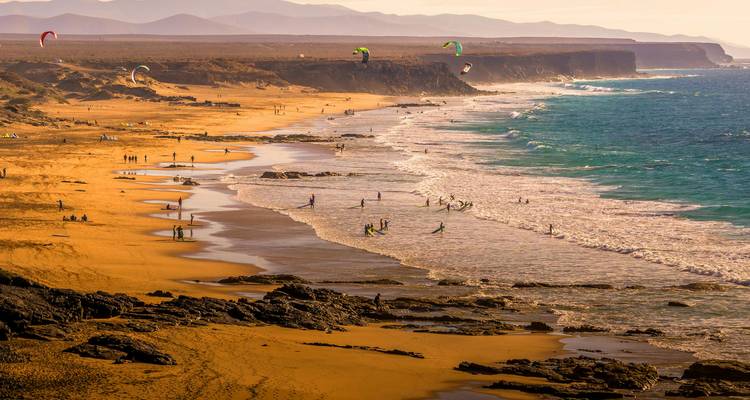 Aussicht zur goldenen Stunde auf eine raue Küstenlinie mit Surfern und Strandbesuchern entlang der Küste
