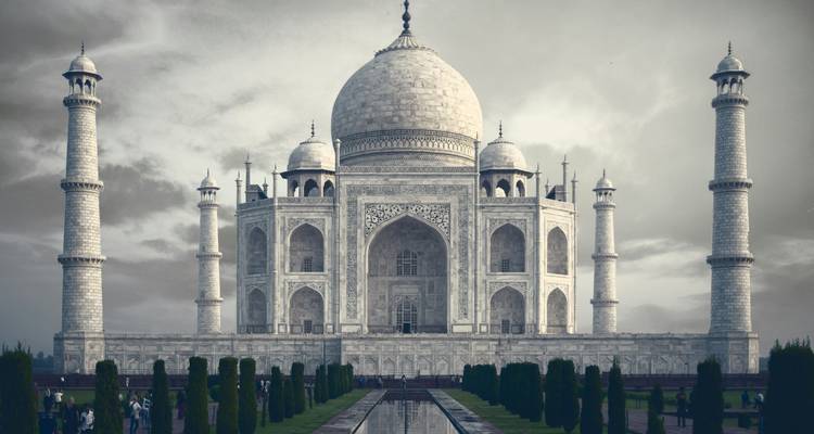 Iconisch marmeren Taj Mahal dat weerspiegeld wordt in zijn lineaire waterbassin onder dramatische bewolkte hemel.