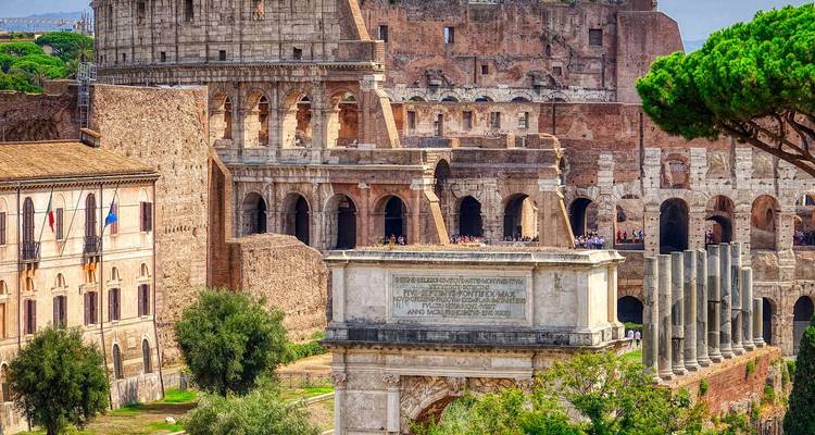 Iconic view of Rome’s Colosseum and Arch of Constantine framed by ancient ruins and cypress trees.