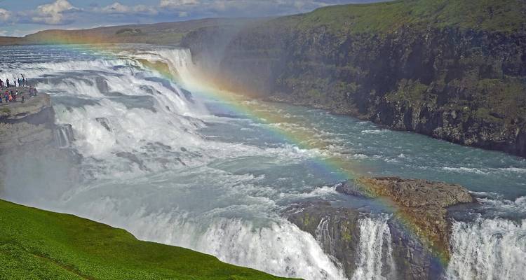 Ein massiver Wasserfall, der in einen felsigen Canyon stürzt, mit einem lebhaften Regenbogen, der sich durch den Nebel spannt.