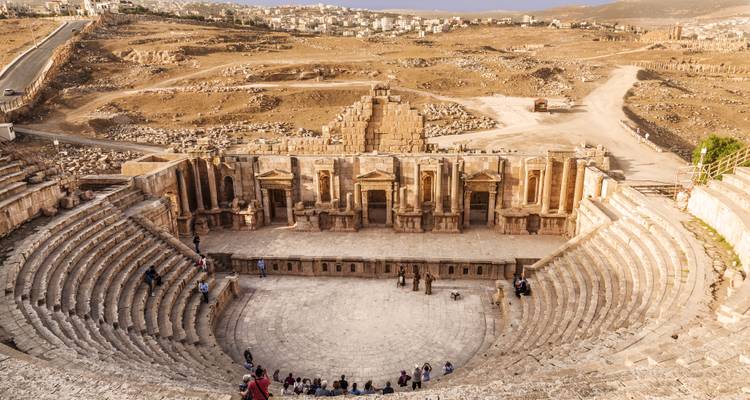 Panoramablick auf das gut erhaltene römische Amphitheater von Jerash mit vereinzelt verteilten Besuchern, die die massiven Steintribünen erkunden.