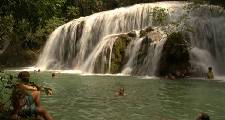 Les baigneurs se détendent dans une piscine turquoise sous une large cascade de jungle qui s'écoule généreusement.