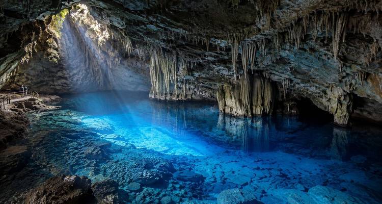 Un rayon de soleil brille dans un lac souterrain bleu à l'intérieur d'une grotte spectaculaire bordée de stalactites.