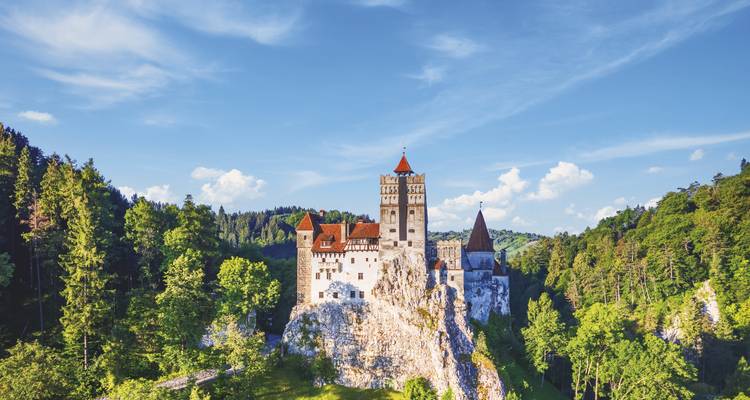 Le château de Bran de conte de fées, perché sur un escarpement rocheux entouré de la luxuriante forêt des Carpates sous un ciel bleu.