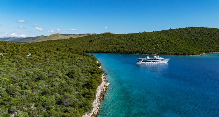Vista aérea amplia de un canal azul con un crucero y una orilla rocosa y verde bajo un cielo despejado.