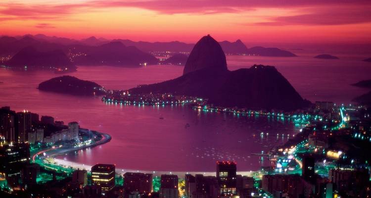 Atardecer vibrante en tonos rosa y púrpura sobre la Bahía de Guanabara con el Pão de Açúcar recortado en silueta y las luces de la ciudad brillando.