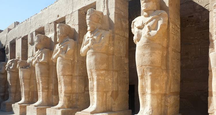 Rows of colossal sandstone statues stand guard along a temple colonnade.