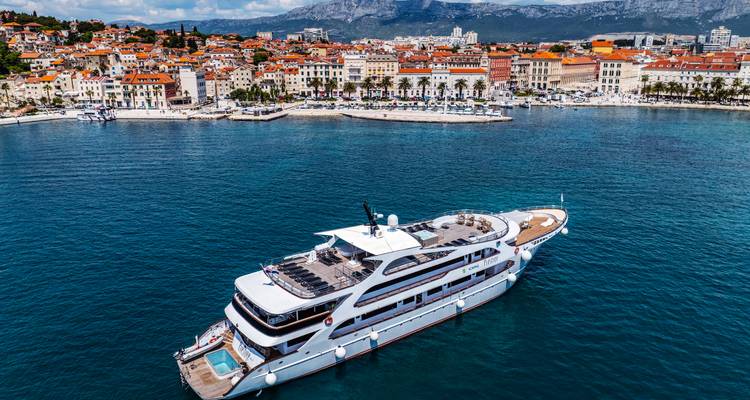 White yacht anchored off Split with the historic Croatian city and mountains behind.