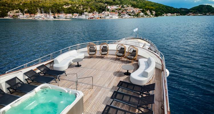 Bow deck with curved sofas and hot tub sailing past forested Croatian coastline.
