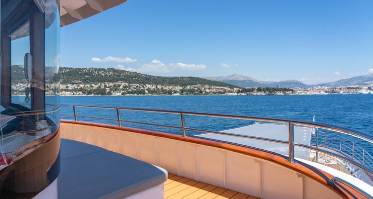 Ship balcony view of Split coastline and mountains under clear blue sky.