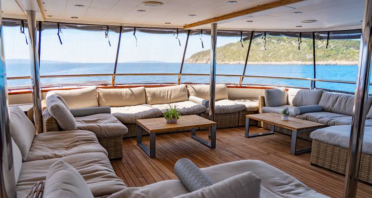 Comfortable shaded lounge area on ship’s aft deck facing turquoise sea and distant shoreline.
