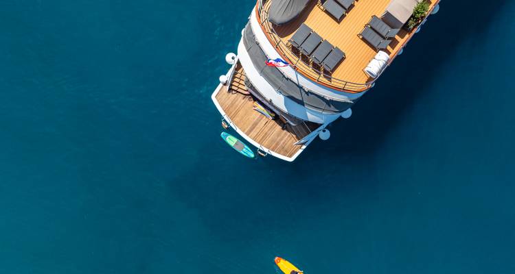 Top-down drone shot of yacht stern with paddleboard floating on deep blue sea.