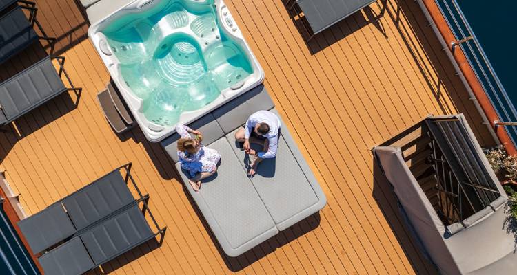 Overhead shot of couple relaxing on padded sun deck platform beside jacuzzi.