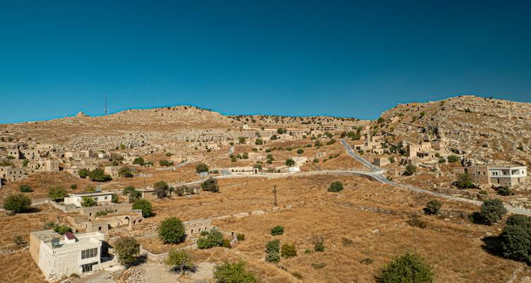 Arid hillside dotted with abandoned stone houses beneath a deep blue sky in eastern Turkey.