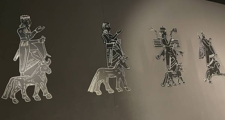 Stylized monochrome illustrations of ancient Near Eastern figures displayed on a dark museum wall.