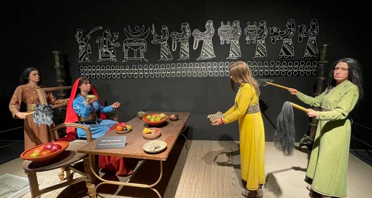 Museum diorama with life-size mannequins in historical dress gathered around a wooden table of food.