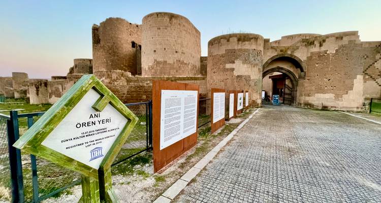 UNESCO sign and information panels at the fortified entrance of Ani ruins during twilight.
