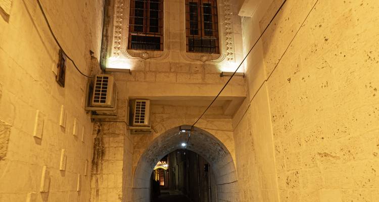 Narrow stone alleyway with arched passage lit by warm lights in an old Turkish town at night.