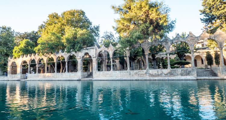 Une colonnade de pierre en arcades se reflète dans les eaux turquoise d'un bassin sacré bordé de poissons.
