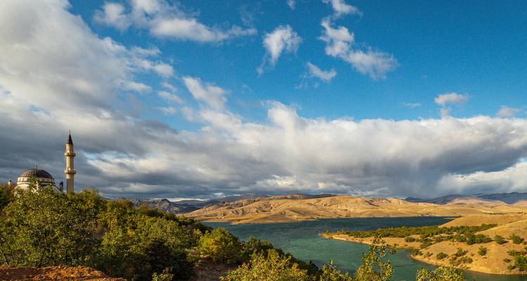 Le minaret s'élève au-dessus de collines verdoyantes à côté d'un lac agité par le vent sous des nuages dramatiques.
