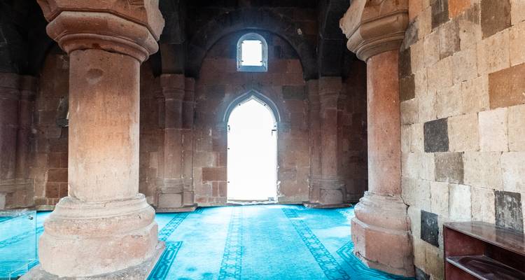 Des colonnes en pierre et une porte cintrée à l'intérieur d'une ancienne église illuminées par une lumière douce.