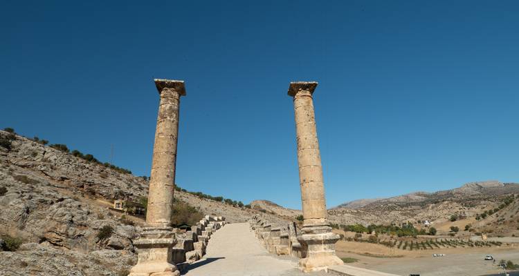 Deux anciennes colonnes de pierre se dressent seules au sommet d'un large escalier contre un ciel bleu dégagé.