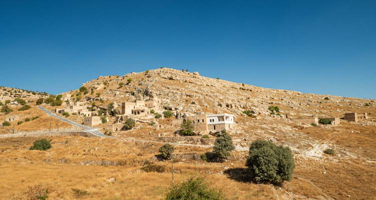 Versant exposé au soleil parsemé de maisons en pierre et de ruines sous des ciels bleus sans nuages.