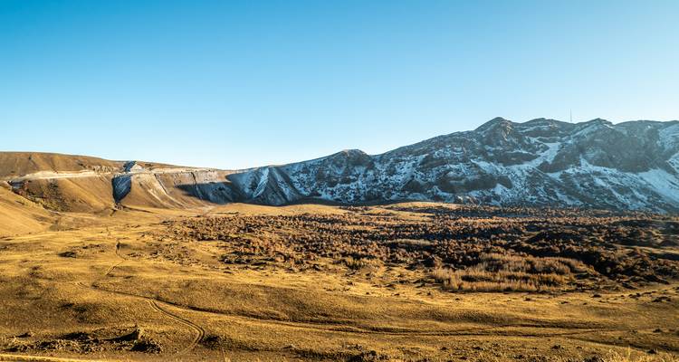 Vaste plateau d'altitude élevée aux herbes dorées, bordé par un massif volcanique parsemé de neige.