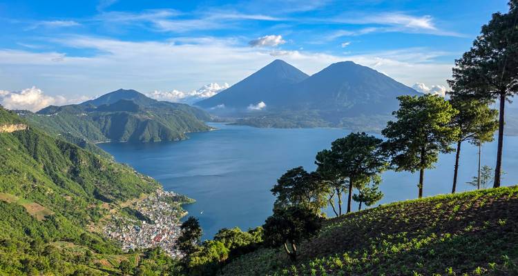 Panoramic view over Lake Atitlán with twin volcanoes and green terraces descending to a lakeside village