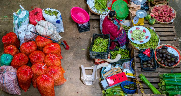 Overhead view of a bustling market stall with colorful vegetables, sacks and a vendor in traditional dress