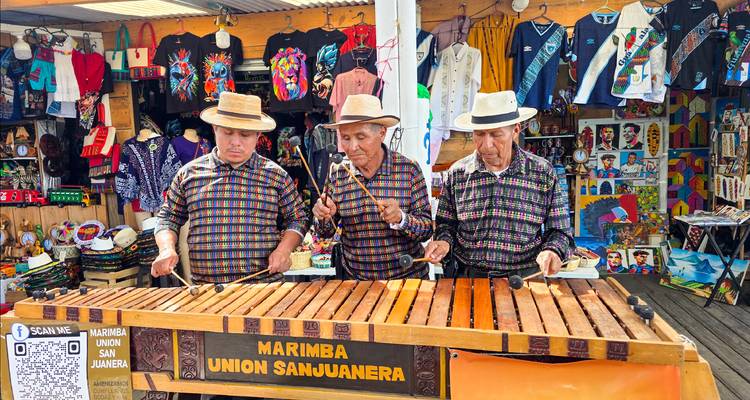 Three elderly musicians in traditional shirts play a wooden marimba at a colorful craft market stall
