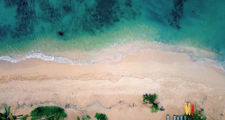 Top-down drone view of turquoise waves lapping a secluded sandy beach with kayaks on shore.