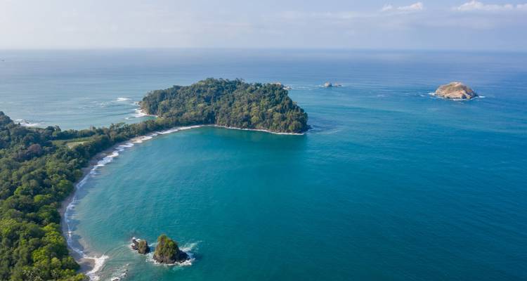 Panorama aérien d'une baie en forme de croissant et d'îlots entourés de forêt tropicale et de mer turquoise