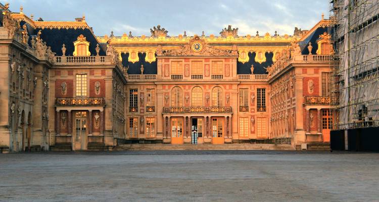 La lumière dorée du matin illuminant la façade ornée de la cour principale du Palais de Versailles.