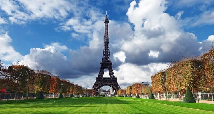 Vue classique de face de la Tour Eiffel s'élevant au-dessus d'une pelouse verte soigneusement entretenue sous un ciel dramatique.