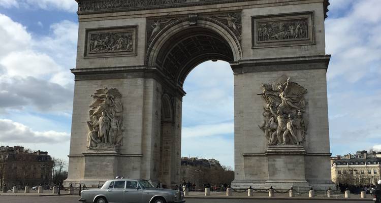 Monument en pierre de l'Arc de Triomphe sous un ciel partiellement nuageux avec une voiture vintage au premier plan.