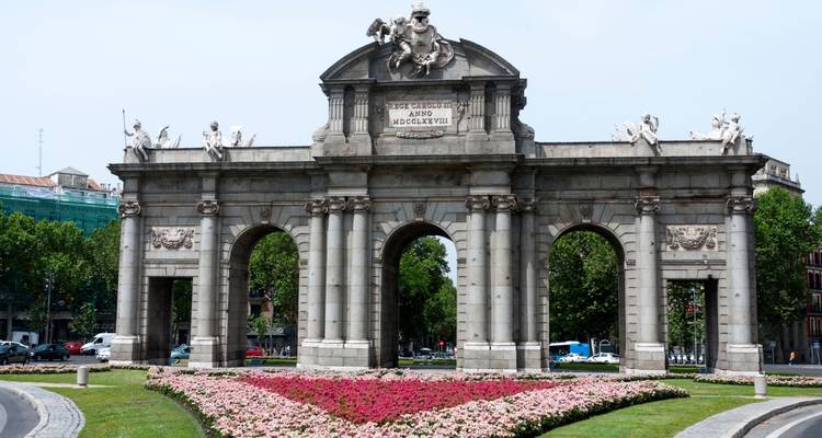 Frontansicht des Puerta de Alcalá mit kreisförmigen Blumenbeeten und leichtem Verkehr in der Umgebung