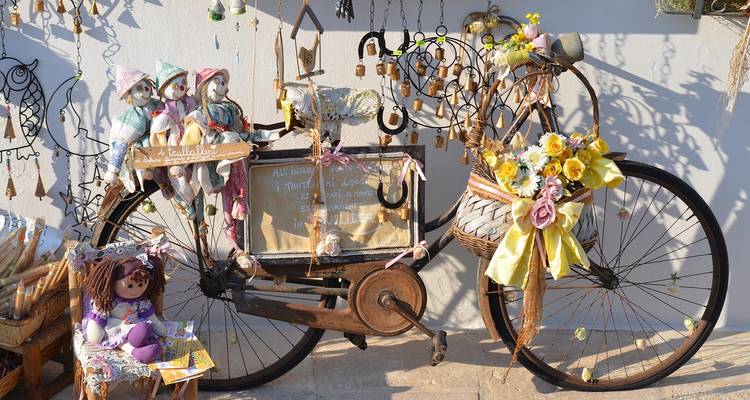 Vélo vintage décoré de poupées, de fleurs et de bibelots appuyé contre un mur blanc