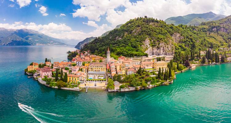 Aerial panorama of colorful Varenna village on Lake Como surrounded by green mountains.