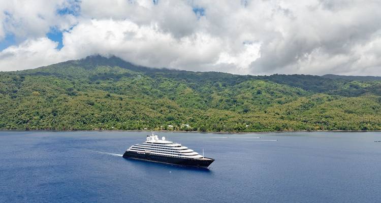 Croisière en yacht d'expédition de luxe dans des eaux d'un bleu profond avec un décor d'île volcanique verdoyante.