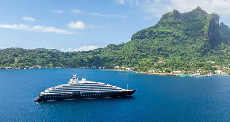 Yacht d'expédition de luxe ancré dans un lagon bleu profond sous une île volcanique luxuriante