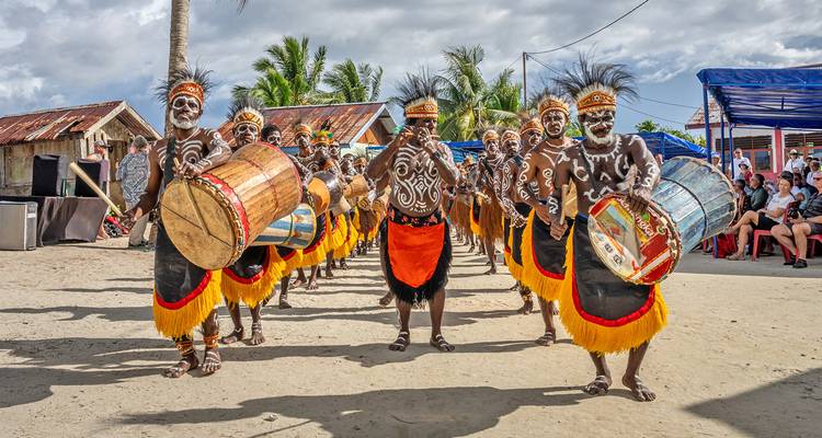 Rangée de danseurs traditionnels vêtus de costumes tribaux aux couleurs éclatantes jouant de grands tambours en bois lors d'une célébration villageoise en plein air.