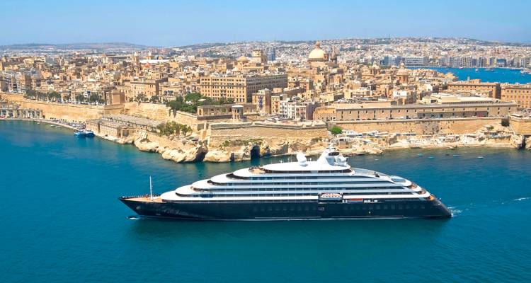 Sleek luxury yacht cruising past the golden limestone skyline of Valletta's historic harbor