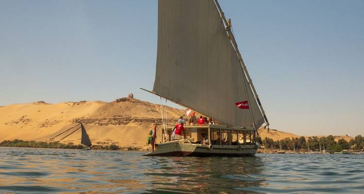 Felouque traditionnelle avec une grande voile glissant sur le Nil à côté des dunes dorées du désert.