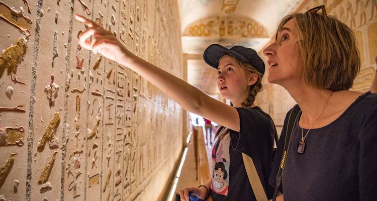 Deux visiteurs étudiant des hiéroglyphes colorés à l'intérieur d'un corridor de tombeau égyptien ancien.