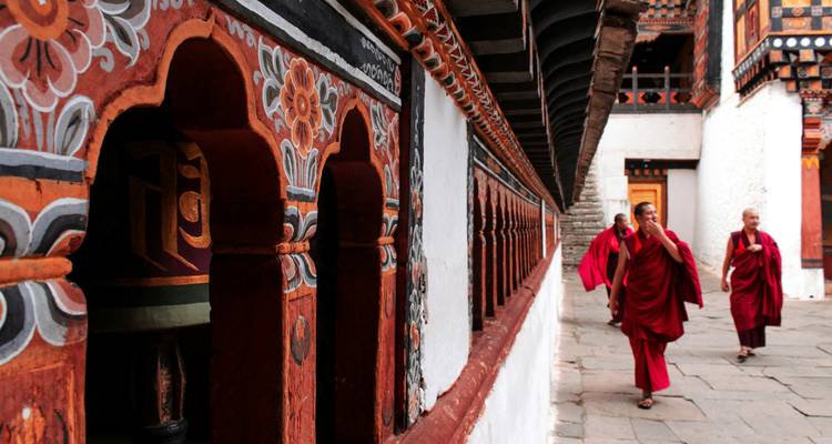Monks in red robes walking along vibrantly painted temple corridor with ornate patterns