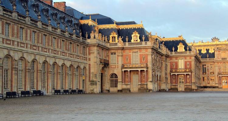 Long wing of the Palace of Versailles with ornate stone columns and dormer windows glowing in soft light.