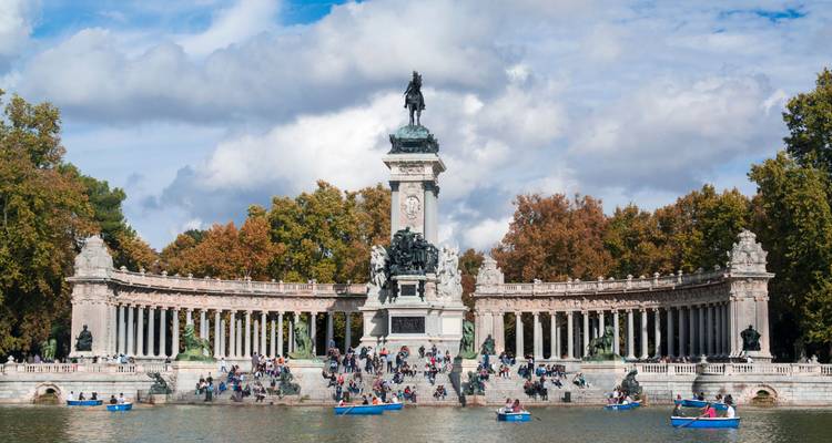 Monument to Alfonso XII in Madrid’s Retiro Park with boating lake crowded with rowboats and visitors.