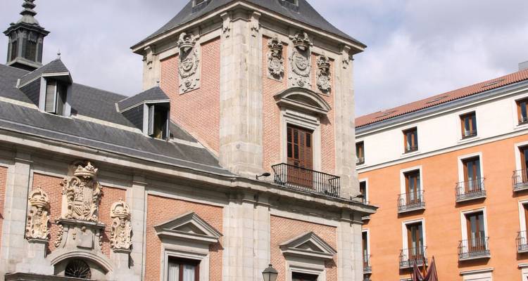 Historic brick and stone civic building with heraldic crest in Madrid’s old town under light clouds.