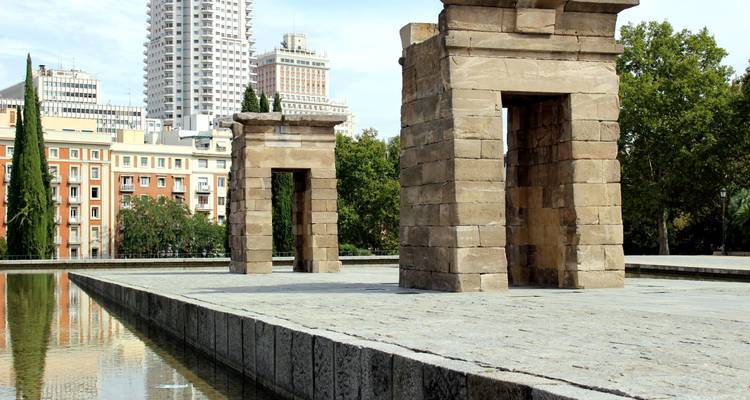 Ancient Egyptian Temple of Debod reflected in a water pool with Madrid city buildings in background.